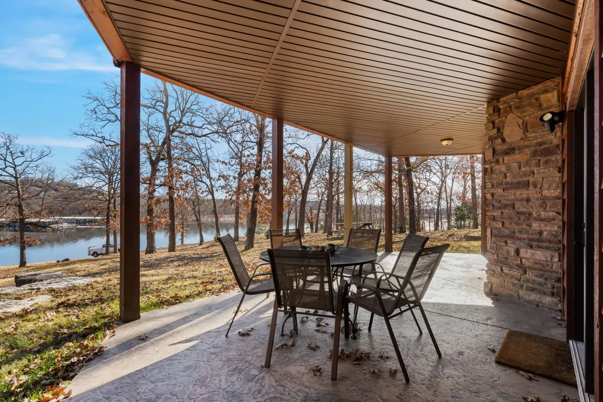 An inviting outdoor setup featuring a table and chairs looking out over the peaceful lake, surrounded by trees. The scene is tranquil, perfect for outdoor dining or relaxing with a pet by your side.