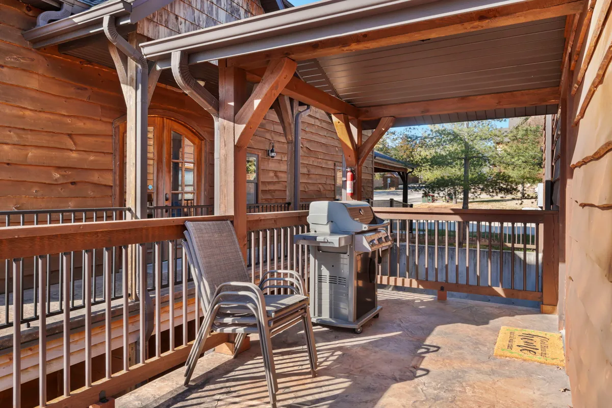 The image features an outdoor grill and seating area on a wooden deck, with a view of the lake beyond the railing. The scene suggests the potential for lively barbecues and outdoor dining, inviting groups to gather and enjoy meals together in a scenic setting.