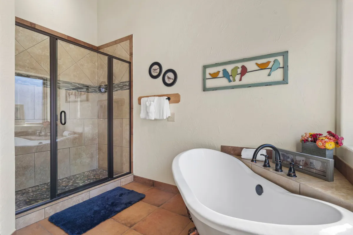A bright bathroom scene centered on a freestanding bathtub and a glass shower enclosure, complemented by colorful bird artwork. The space feels tranquil and luxurious, evoking the spa-like features of the master suites.