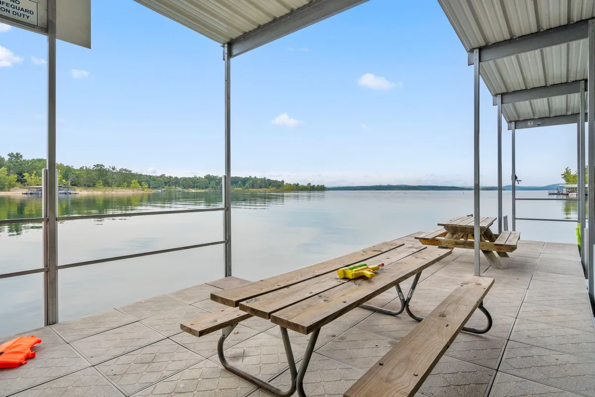 An inviting lakeside scene featuring picnic tables overlooking the water and a casual lounge area, suggesting a spot for both relaxation and shared meals. The setting is ideal for picnicking, enjoying the view, or preparing for a day of lake activities.