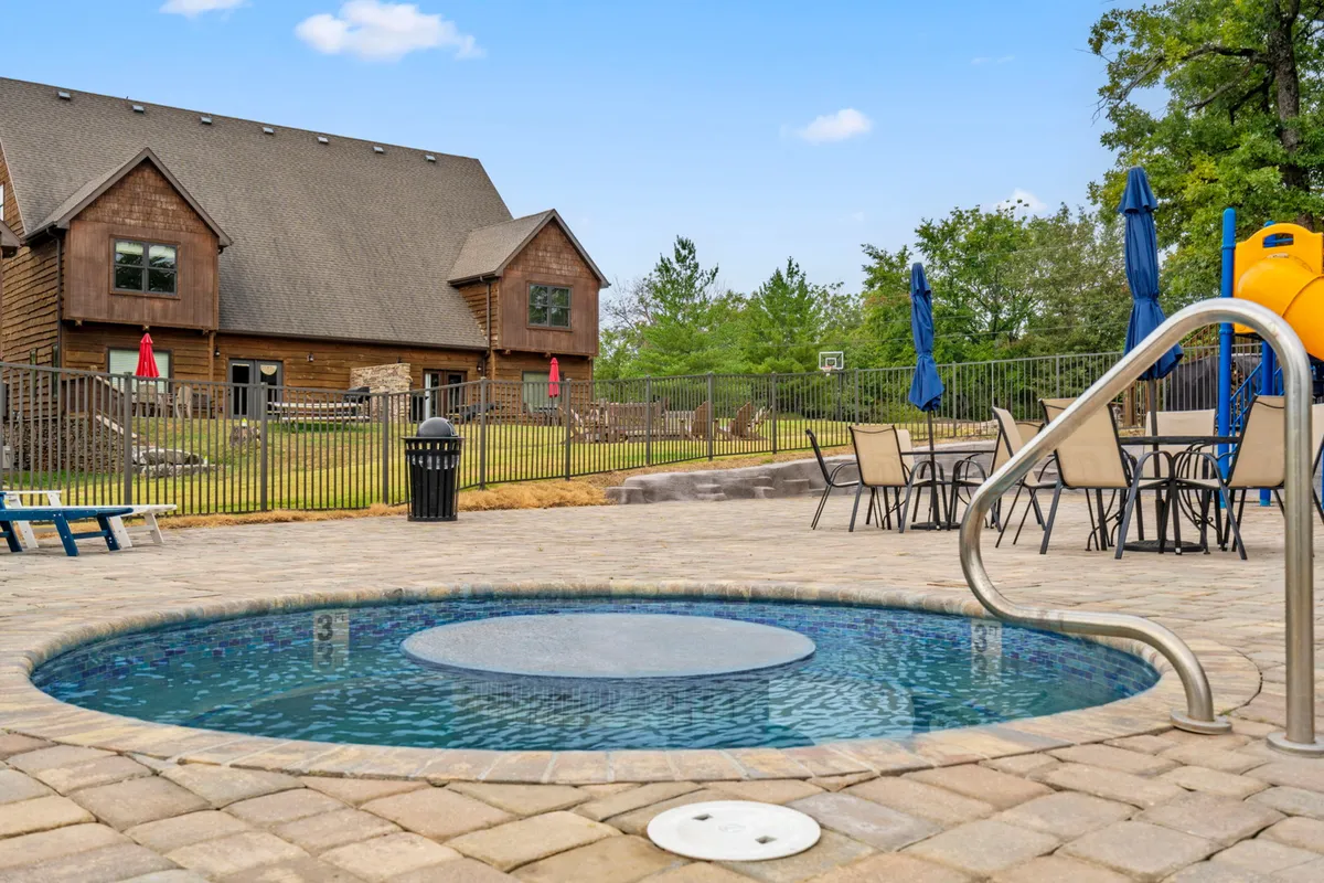 A multi-featured outdoor area with a hot tub, patio seating, a playground slide, a pool area, and the house exterior. The scene captures various activities: swimming, relaxing in the hot tub, outdoor dining, and children playing—all in one vibrant, family-friendly setting.