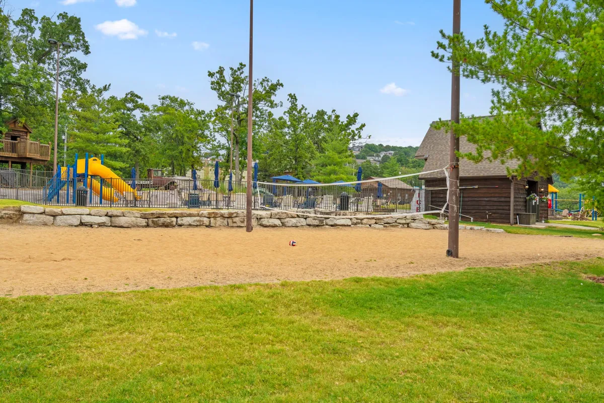 Set in a green, tree-lined outdoor space, this image features playground equipment, a sand volleyball court, and a playhouse structure. Families and children are seen engaging in sports, games, and social gatherings, illustrating a lively and energetic community environment.