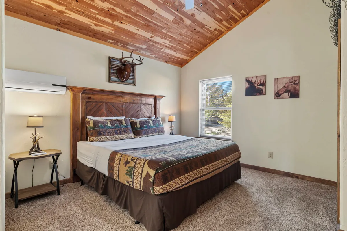 A queen bedroom with a wooden headboard, decorative pillows, and rustic antler wall decor. Soft lighting and a nearby side table with a lamp create a warm, restful retreat for adults or teens.
