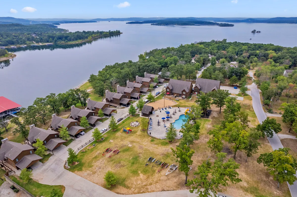 A vibrant lakeside scene with a swimming pool, cabins nestled among greenery, and expansive views of the water. The image showcases people enjoying summer activities such as swimming, boating, hiking, and picnicking, set against a relaxing natural backdrop.