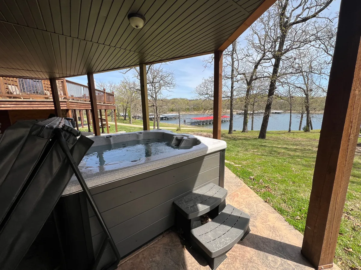 An outdoor patio on the lower level, featuring a private hot tub overlooking the tranquil lake. Steps lead down from the patio, offering both serene relaxation and direct access to outdoor adventures.